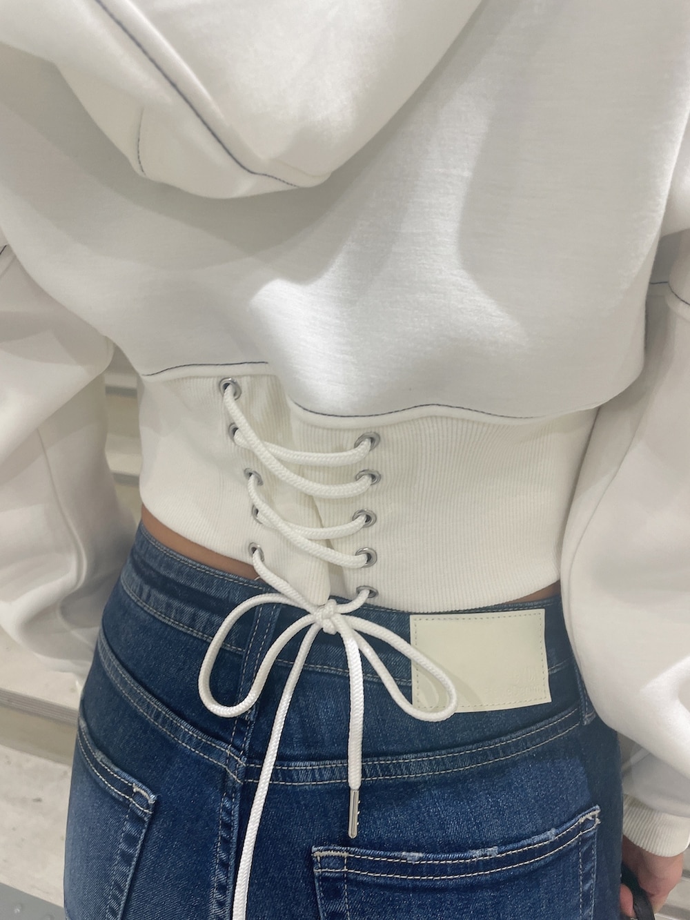 ブラック系のブーツ、ホワイト系のパーカー、ブルー系のデニムパンツを着用したレディースの秋コーディネートの6枚目の写真