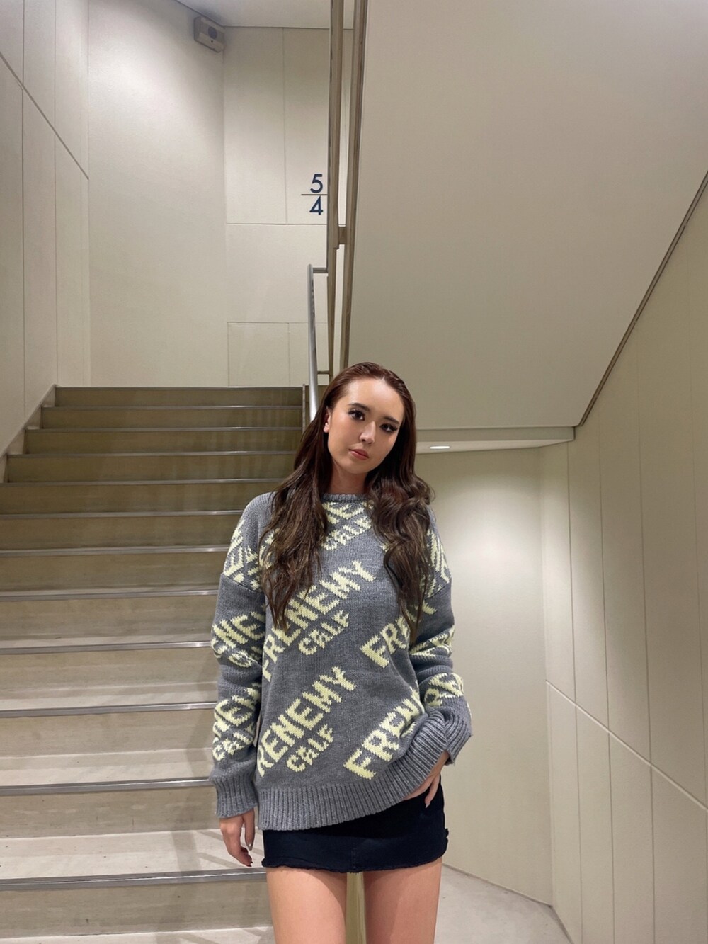 グレー系のニット/セーター、ブラック系のスカート、ブラック系のブーツを着用したレディースの秋コーディネートの3枚目の写真