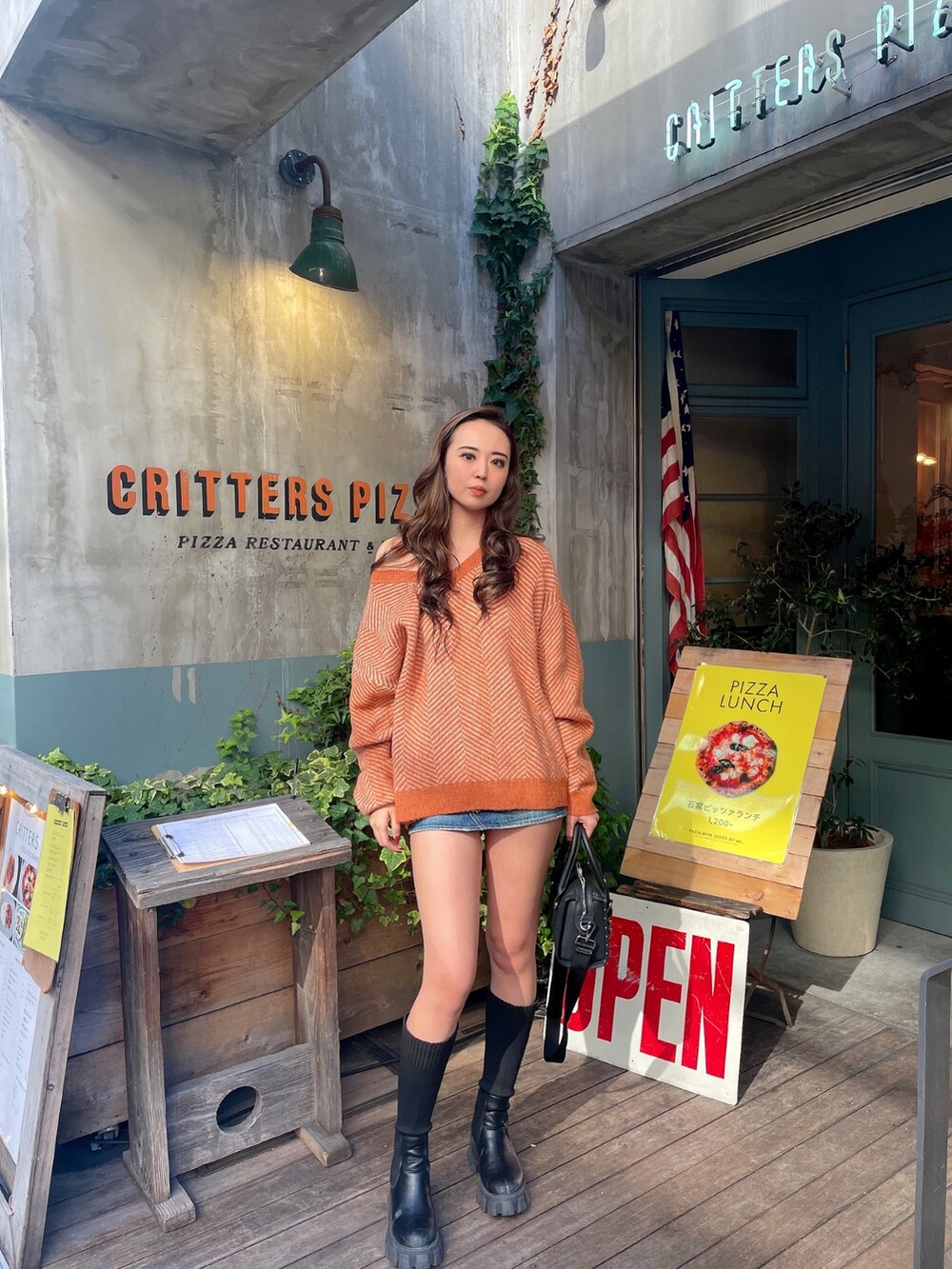 ブルー系のデニムスカート、ブラック系のボストンバッグ、オレンジ系のニット/セーターを着用したレディースの秋コーディネートの2枚目の写真