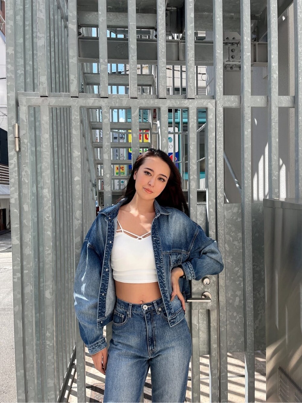 ブルー系のデニムパンツ、ブルー系のデニムジャケット、ホワイト系のキャミソールを着用したレディースの秋コーディネートの2枚目の写真