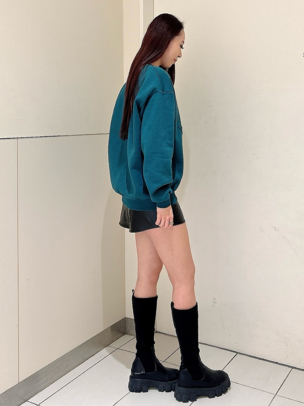 グリーン系のスウェット、ブラック系のスカート、ブラック系のブーツを着用したレディースの冬コーディネートの2枚目の写真