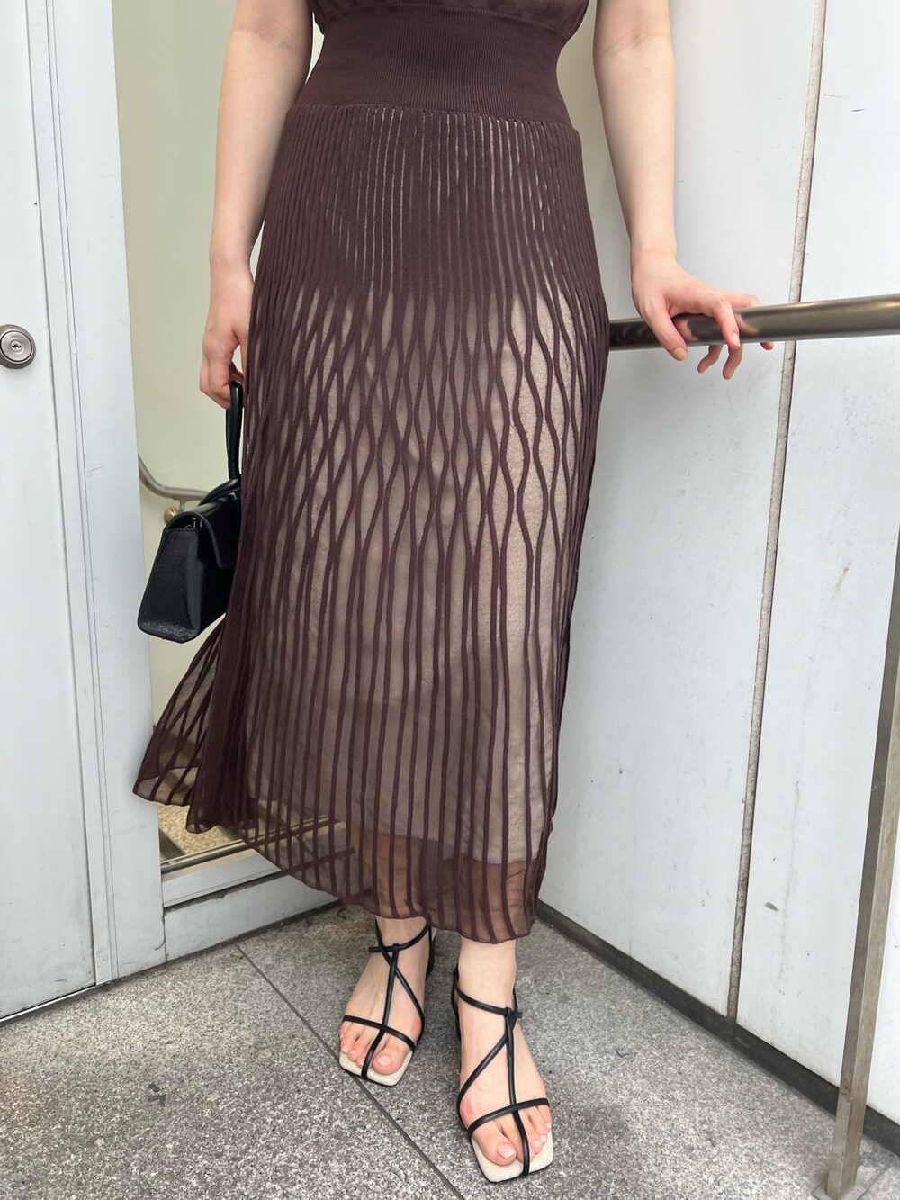 ブラック系のサンダル、ブラック系のハンドバッグ、ブラウン系のワンピースを着用したレディースの夏コーディネートの7枚目の写真