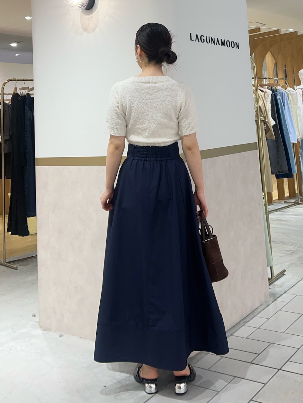 ブルー系のスカート、ホワイト系のニット/セーター、ブラック系のパンプスを着用したレディースの春コーディネートの3枚目の写真