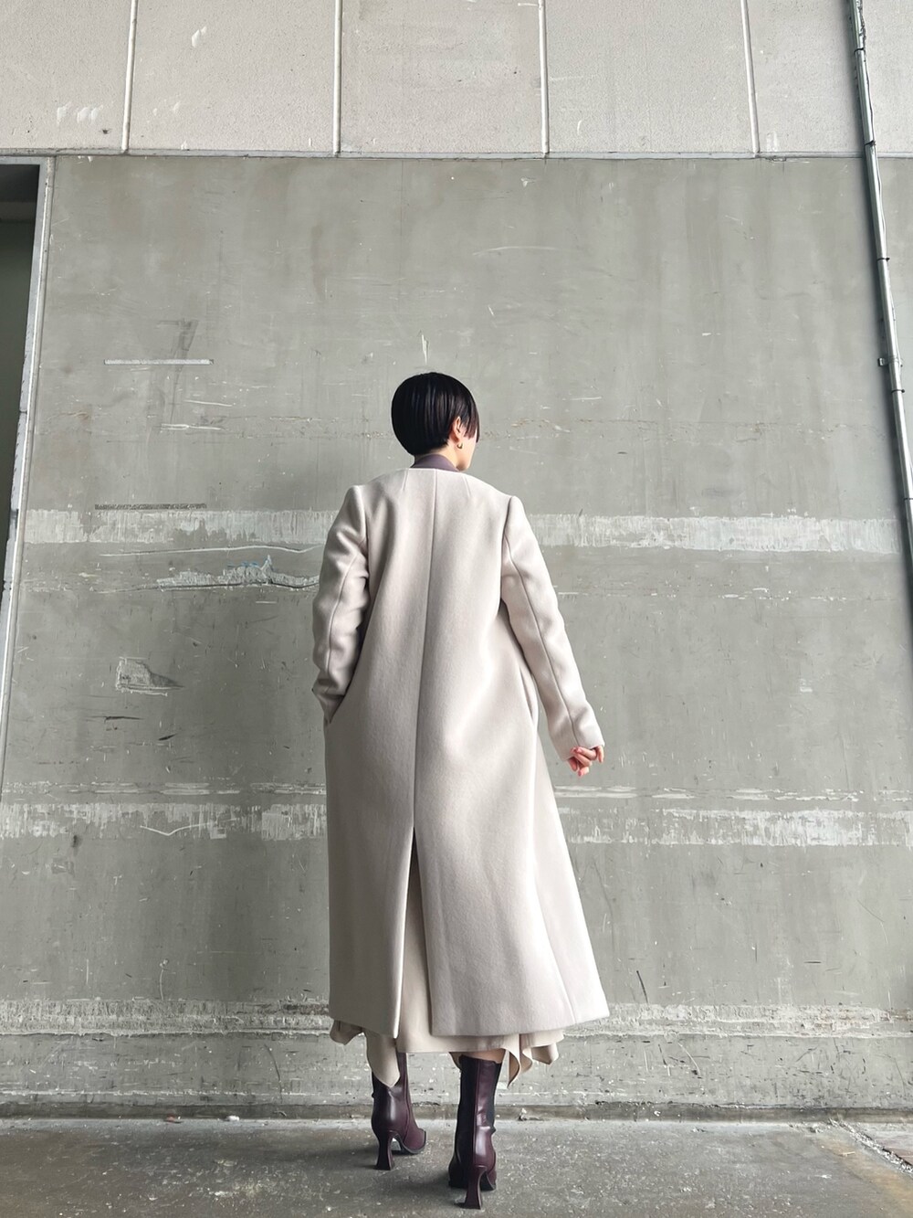 ホワイト系のノーカラーコート、ベージュ系のニット/セーター、ブラウン系のスカートを着用したレディースの秋コーディネートの3枚目の写真