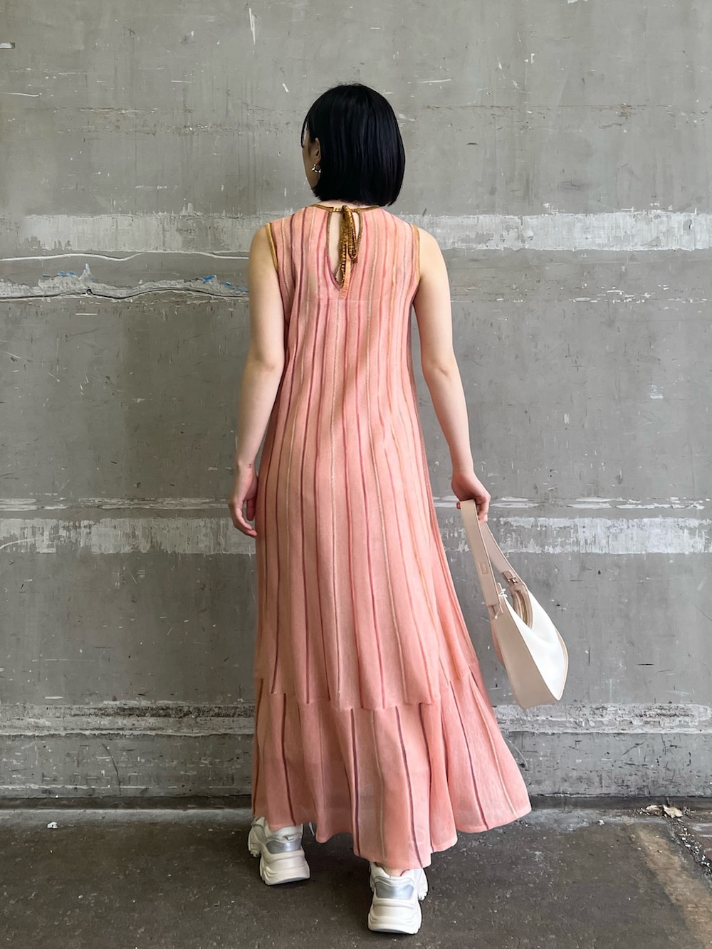 ホワイト系のスニーカー、ベージュ系のハンドバッグ、オレンジ系のワンピースを着用したレディースの春コーディネートの2枚目の写真