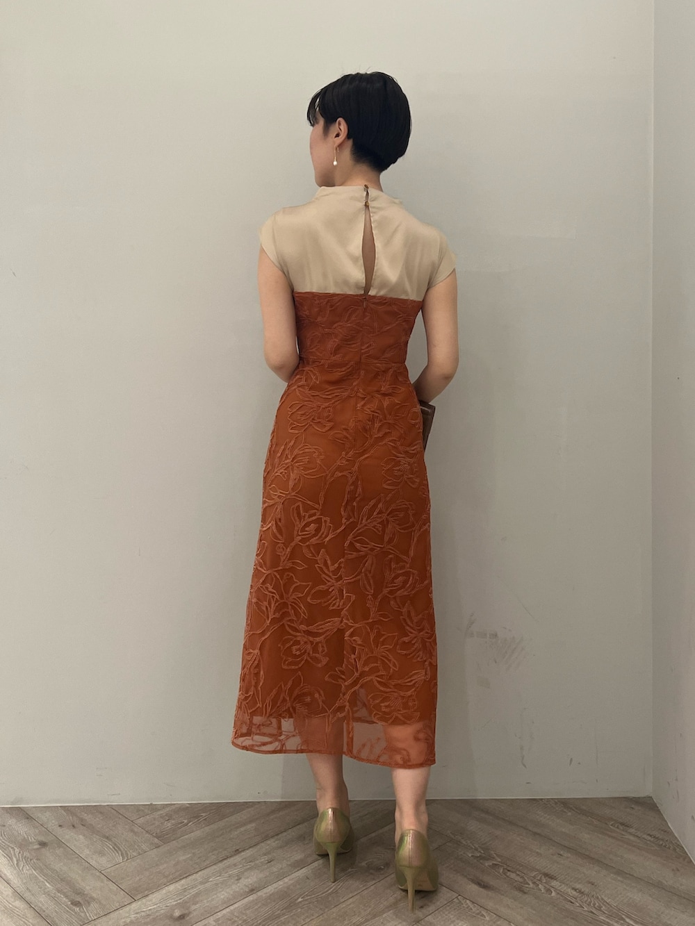 ゴールド系のパンプス、ゴールド系のハンドバッグ、オレンジ系のドレスを着用したレディースの夏コーディネートの2枚目の写真