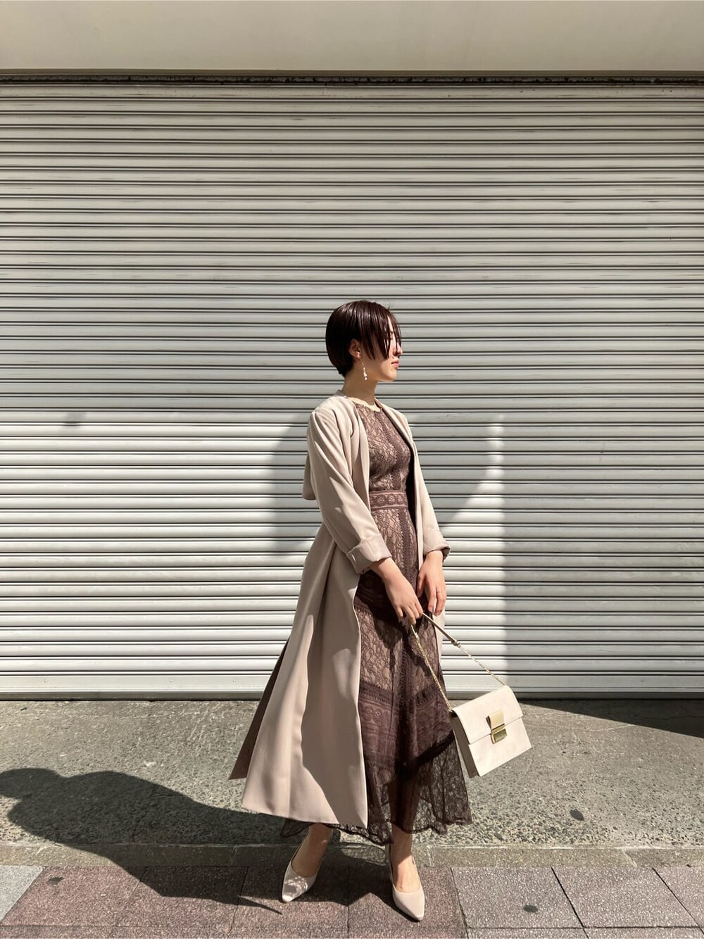 ホワイト系のノーカラーコート、ベージュ系のドレス、ベージュ系のクラッチバッグを着用したレディースの春コーディネートの8枚目の写真
