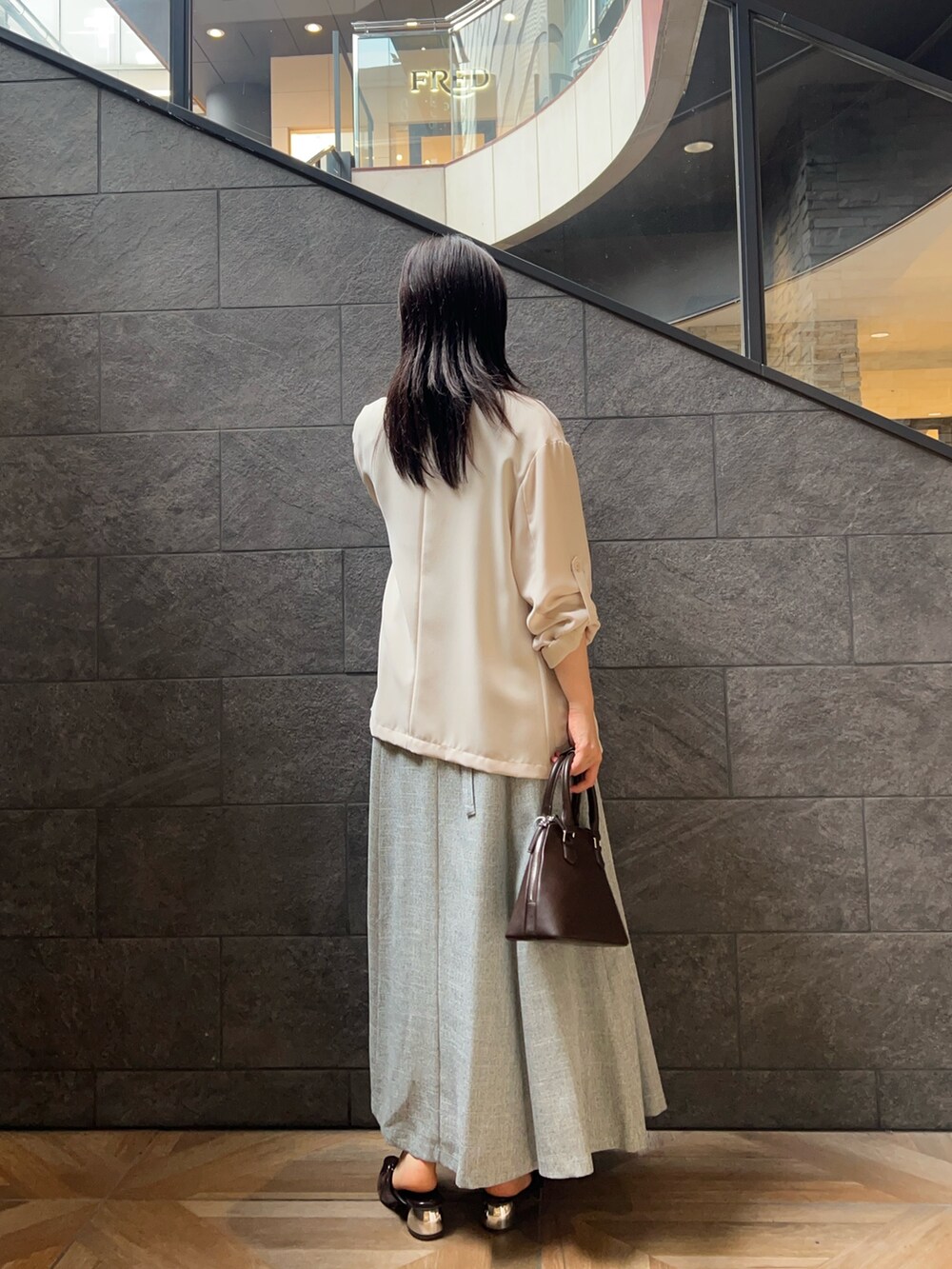 ベージュ系のテーラードジャケット、ブルー系のワンピース、ブラウン系のパンプスを着用したレディースの夏コーディネートの3枚目の写真