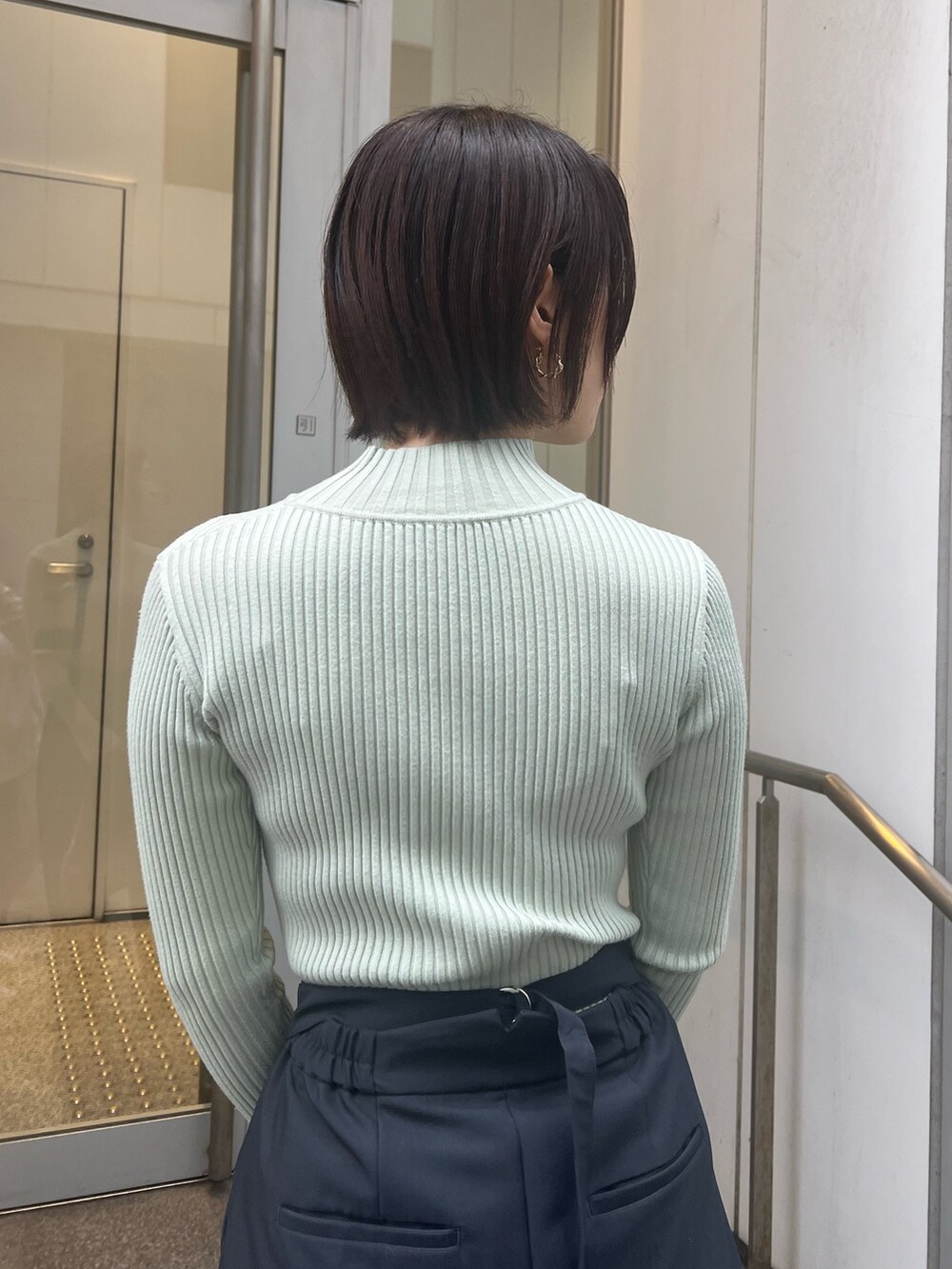 ブルー系のショルダーバッグ、グレー系のスラックス、グリーン系のニット/セーターを着用したレディースの冬コーディネートの5枚目の写真