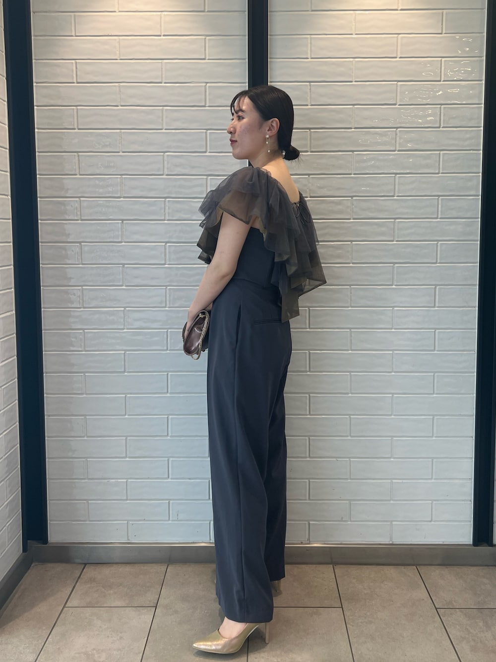 ゴールド系のハンドバッグ、ゴールド系のパンプス、グレー系のパンツドレスを着用したレディースの夏コーディネートの2枚目の写真