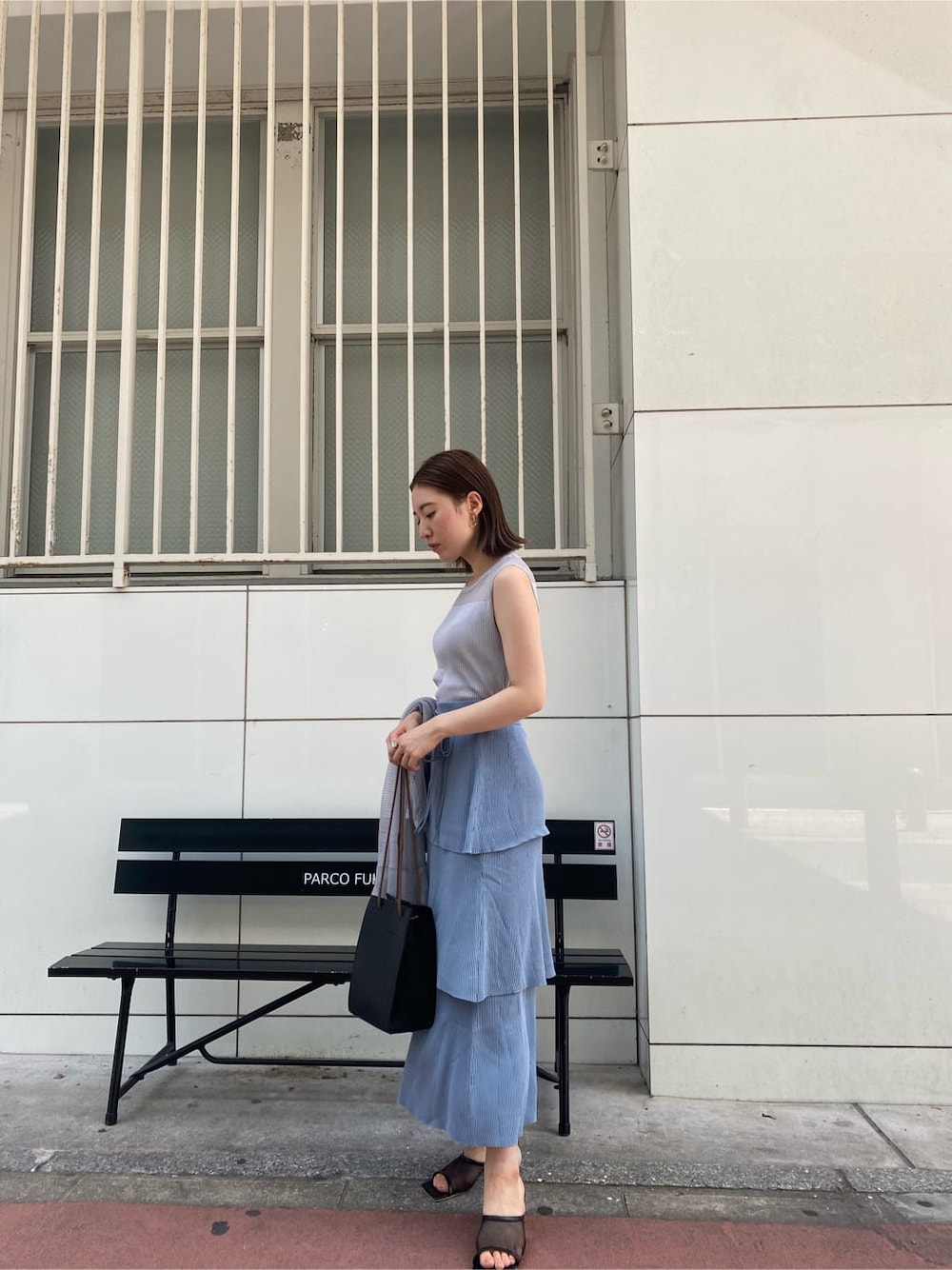 ブラック系のハンドバッグ、ブルー系のスカート、グレー系のニット/セーターを着用したレディースの夏コーディネートの2枚目の写真