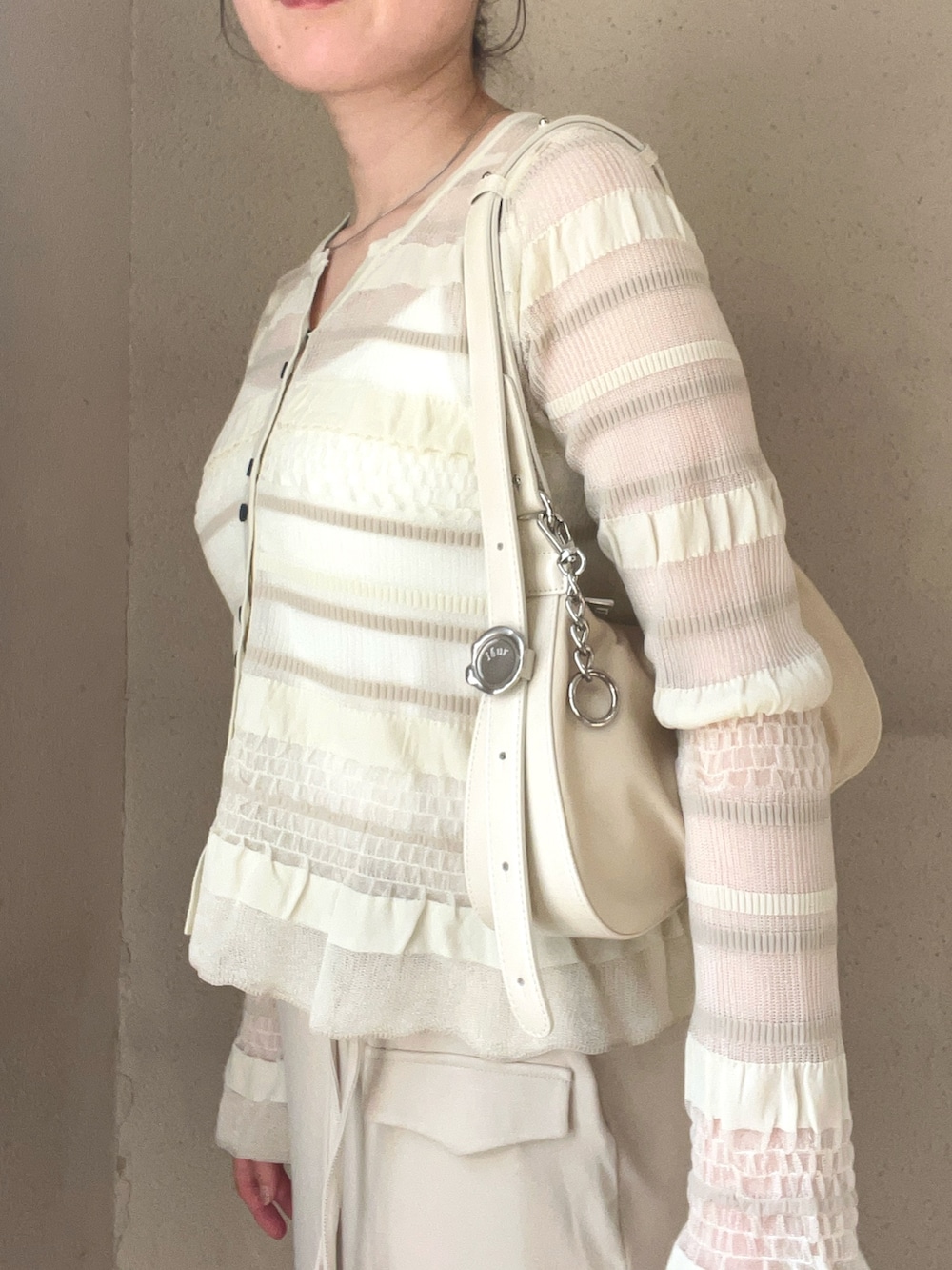 ベージュ系のスカート、ホワイト系のニット/セーター、ホワイト系のスニーカーを着用したレディースの春コーディネートの3枚目の写真