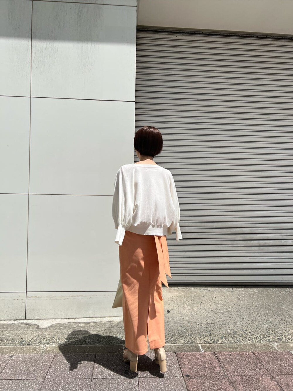 ホワイト系のハンドバッグ、オレンジ系のスカート、その他のパンプスを着用したレディースの春コーディネートの2枚目の写真