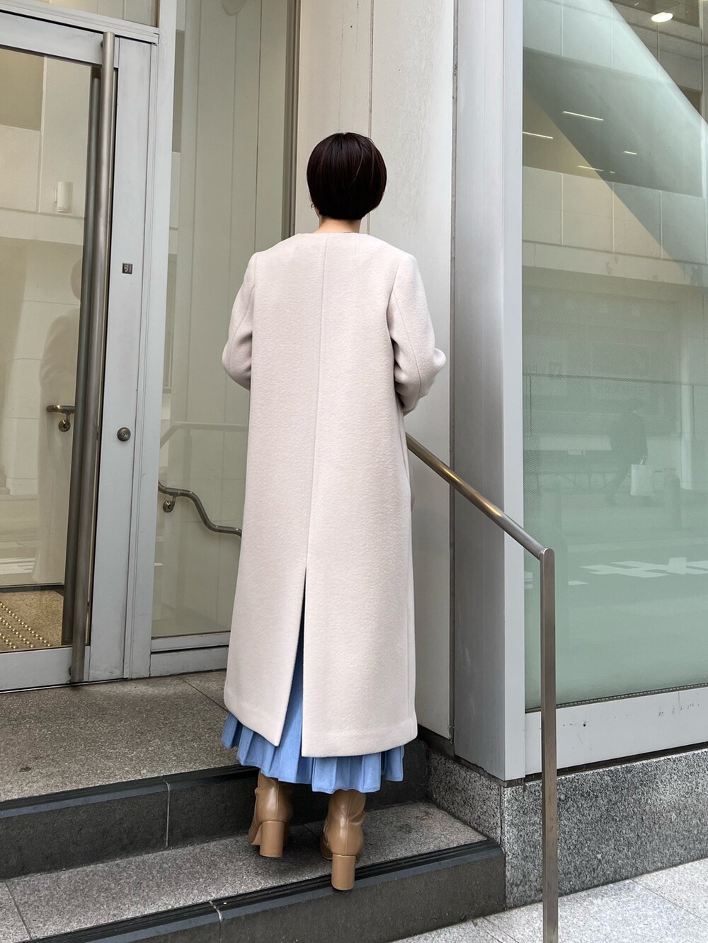 ベージュ系のブーツ、ホワイト系のハンドバッグ、ホワイト系のノーカラーコートを着用したレディースの冬コーディネートの3枚目の写真