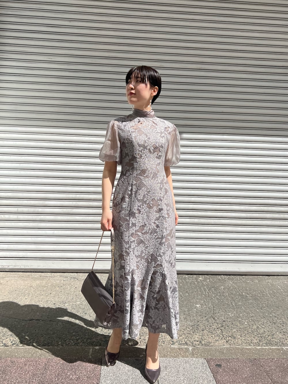 ブルー系のノーカラーコート、シルバー系のパンプス、シルバー系のクラッチバッグを着用したレディースの春コーディネートの3枚目の写真