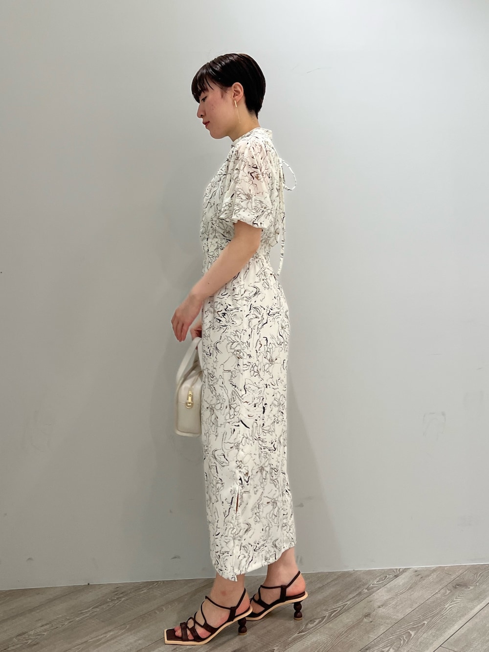 ブラウン系のサンダル、ホワイト系のショルダーバッグ、ホワイト系のワンピースを着用したレディースの春コーディネートの2枚目の写真