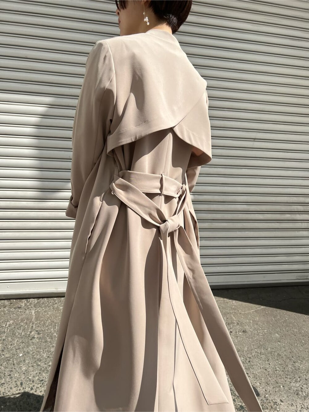 ホワイト系のノーカラーコート、ベージュ系のドレス、ベージュ系のクラッチバッグを着用したレディースの春コーディネートの7枚目の写真