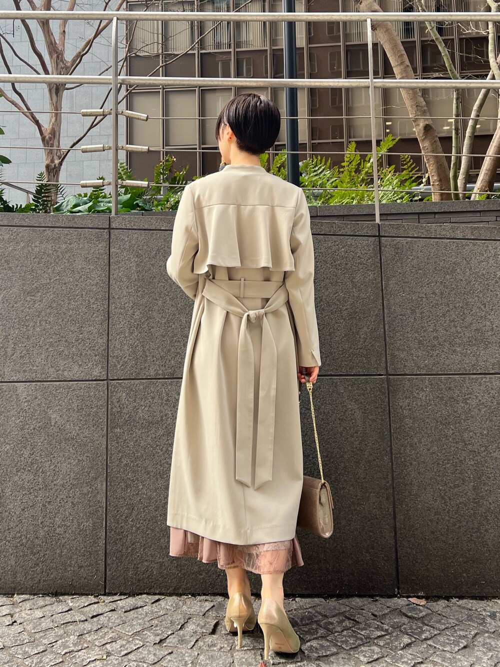ゴールド系のハンドバッグ、ゴールド系のパンプス、ベージュ系のノーカラーコートを着用したレディースの冬コーディネートの2枚目の写真