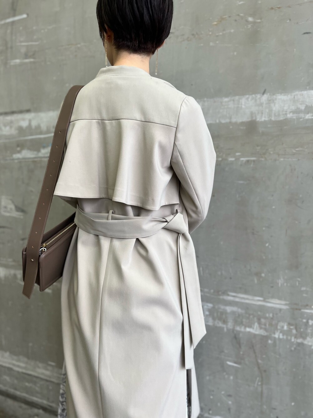 ベージュ系のノーカラーコート、ホワイト系のスカート、ベージュ系のサンダルを着用したレディースの冬コーディネートの3枚目の写真