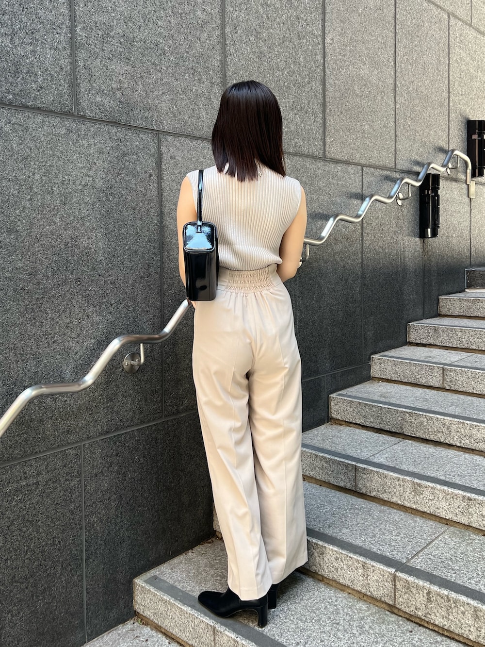 ブラック系のショルダーバッグ、ブラック系のブーツ、ホワイト系のスラックスを着用したレディースの秋コーディネートの4枚目の写真