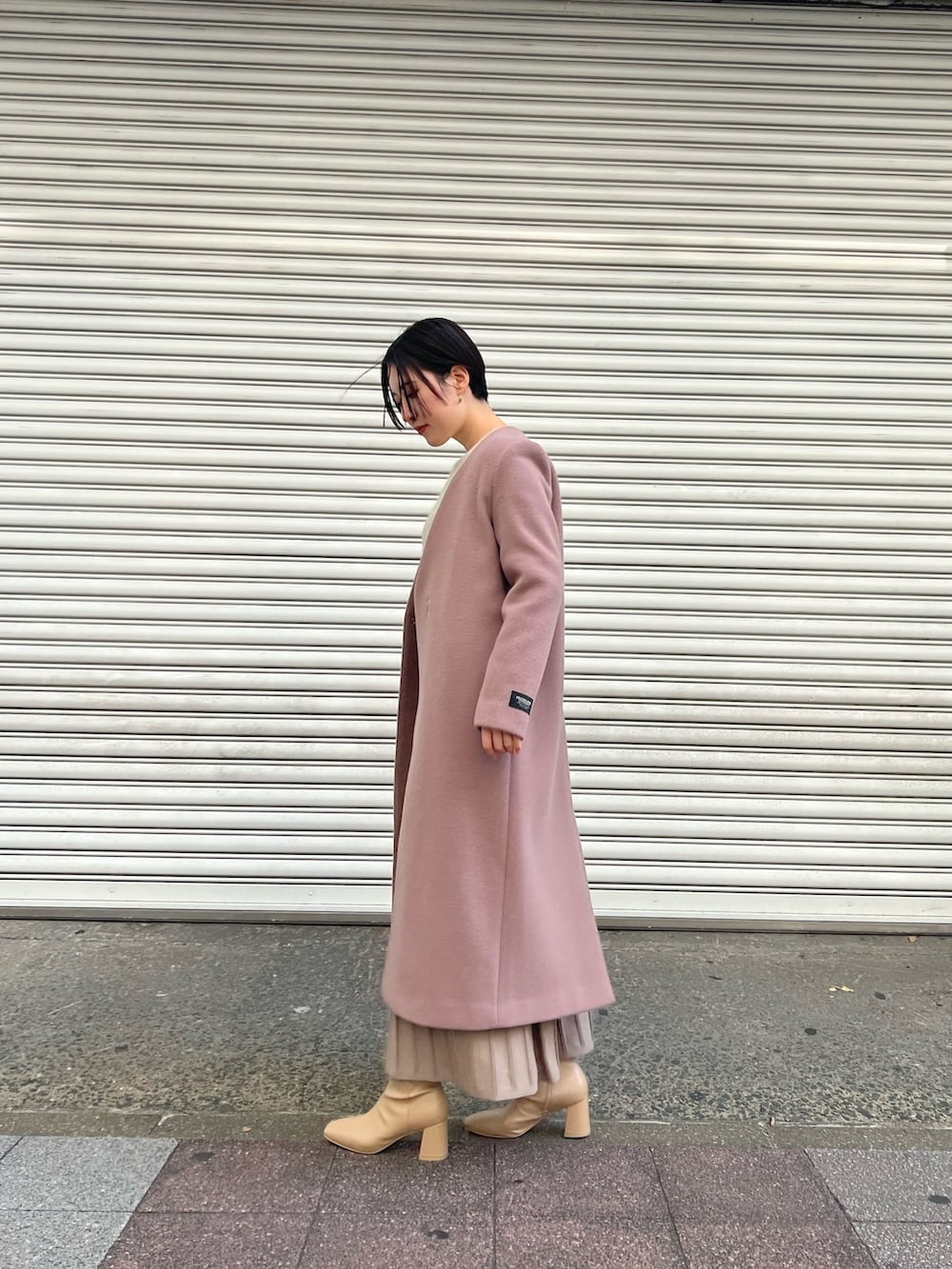 ピンク系のノーカラーコート、ホワイト系のワンピース、ベージュ系のブーツを着用したレディースの秋コーディネートの2枚目の写真