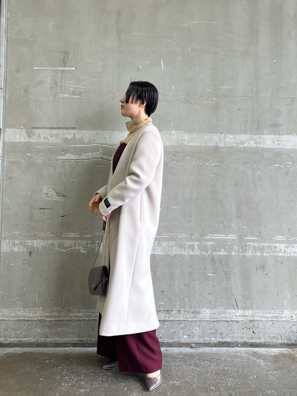 ホワイト系のノーカラーコート、シルバー系のハンドバッグ、シルバー系のパンプスを着用したレディースの冬コーディネートの2枚目の写真