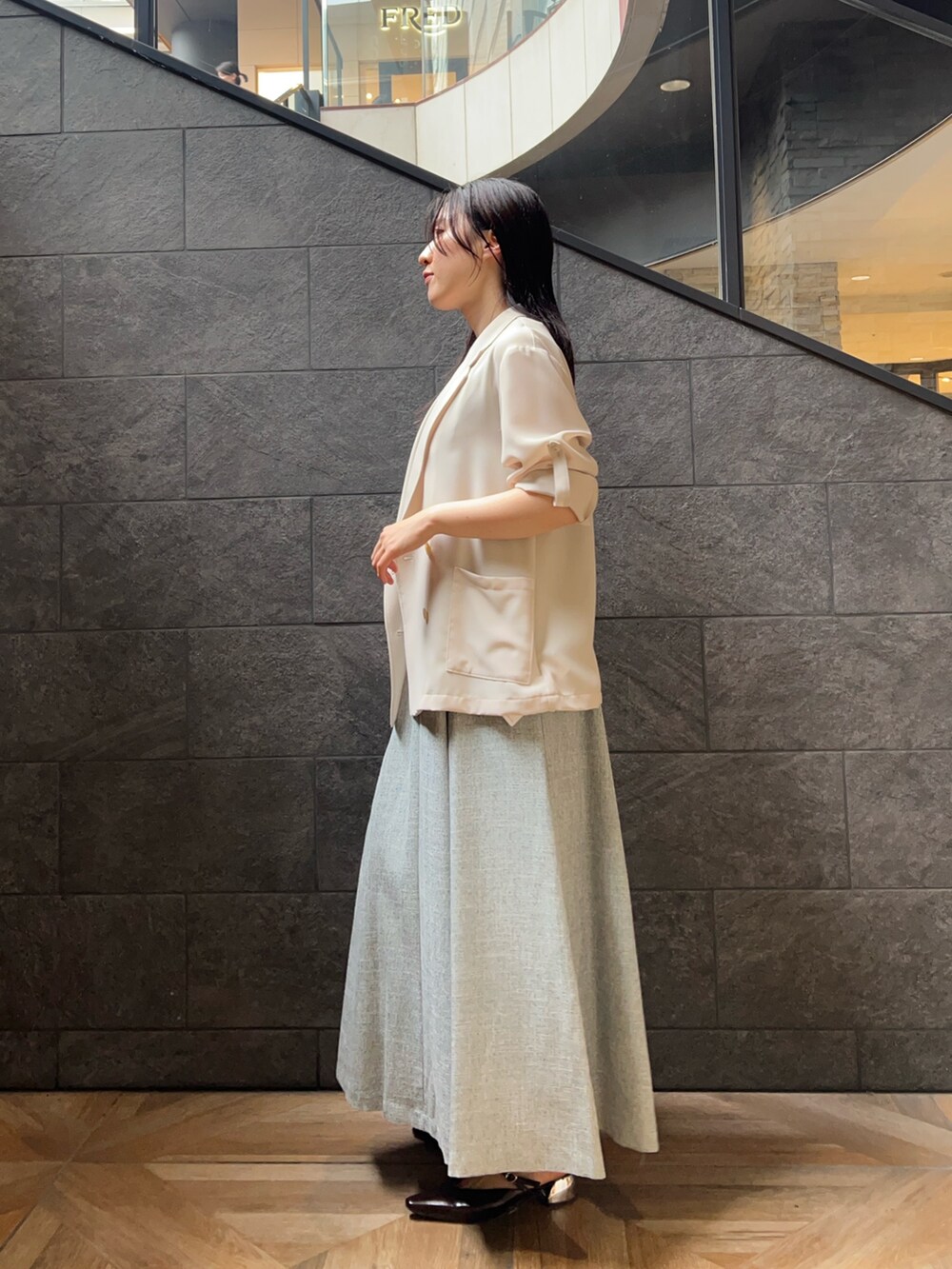 ベージュ系のテーラードジャケット、ブルー系のワンピース、ブラウン系のパンプスを着用したレディースの夏コーディネートの2枚目の写真