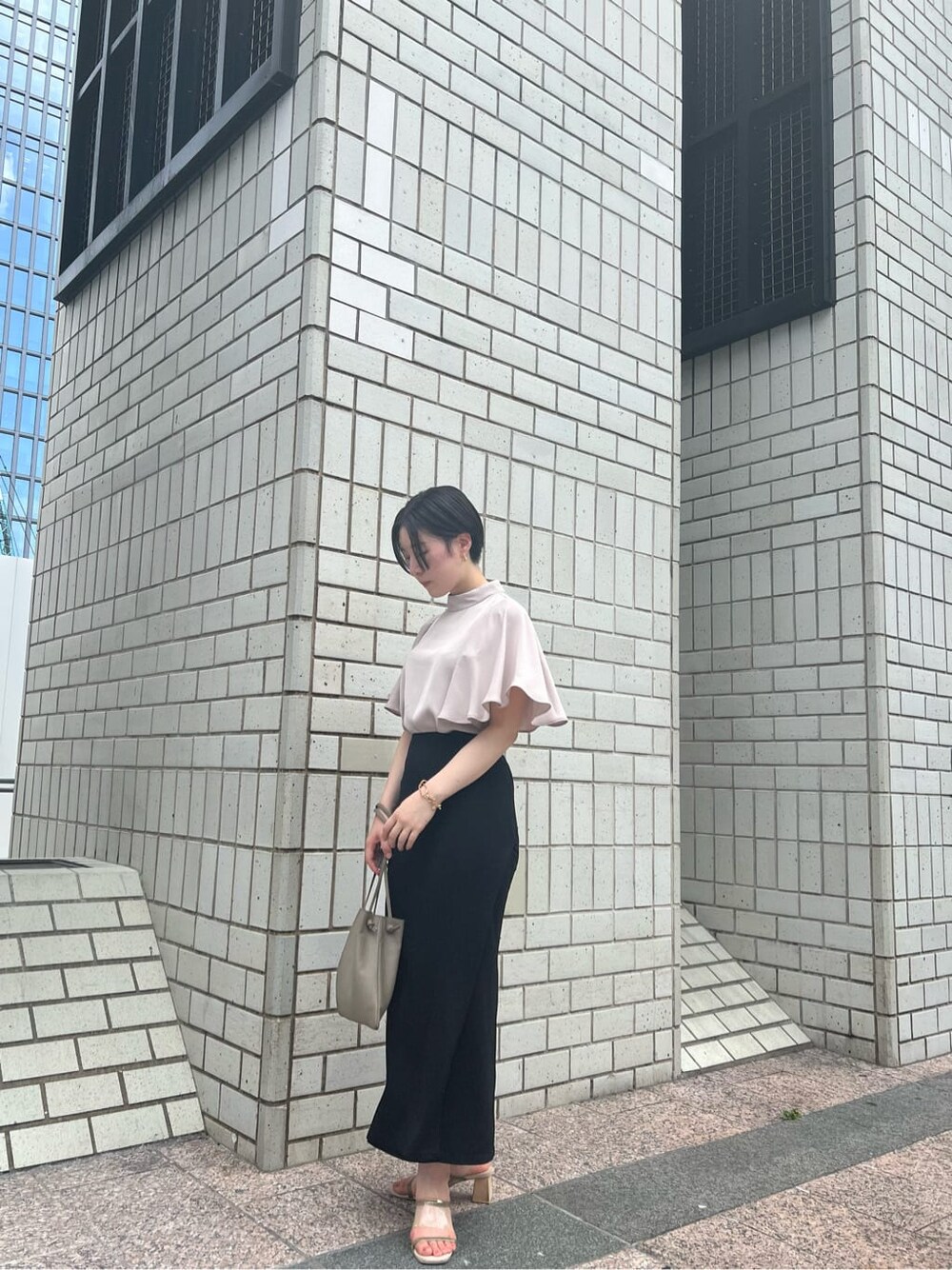 ベージュ系のハンドバッグ、グリーン系のサンダル、ブラック系のスカートを着用したレディースの夏コーディネートの2枚目の写真