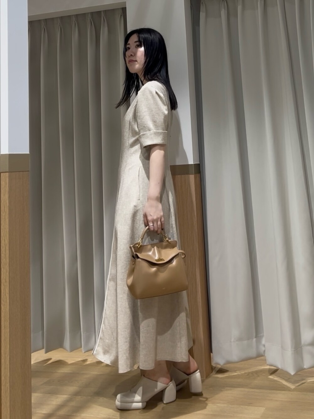 イエロー系のハンドバッグ、ベージュ系のワンピースを着用したレディースの春コーディネートの2枚目の写真