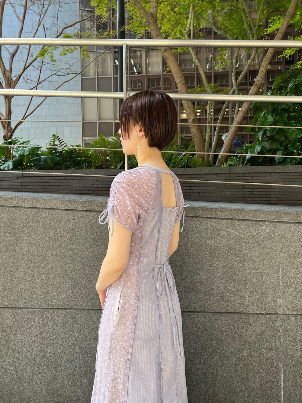 パープル系のドレス、ベージュ系のクラッチバッグ、ベージュ系のパンプスを着用したレディースの春コーディネートの4枚目の写真