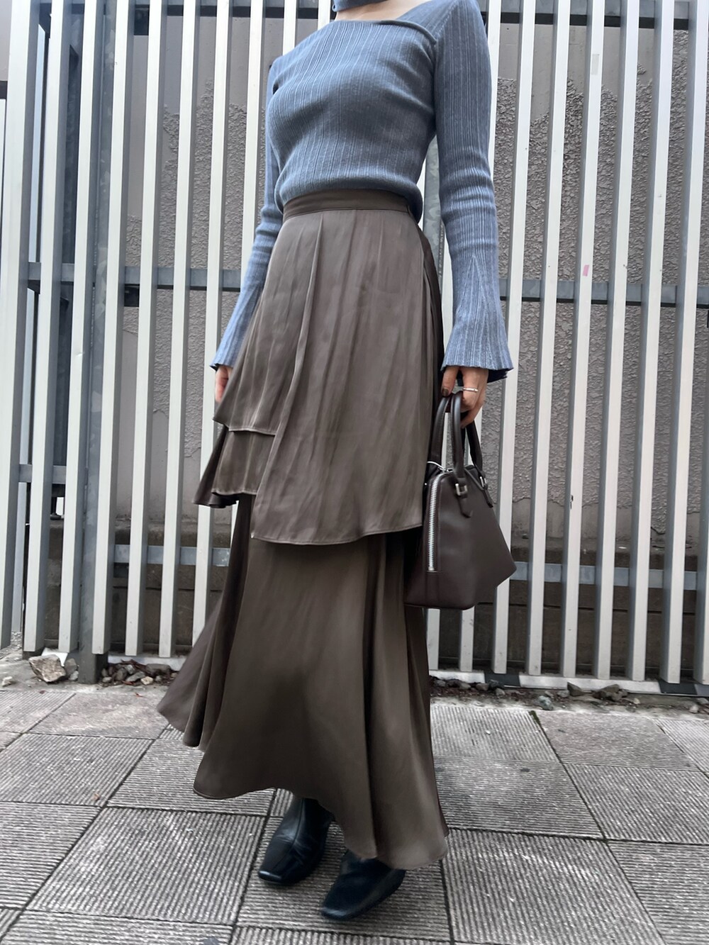 ブルー系のニット/セーター、ブラウン系のスカート、ブラック系のブーツを着用したレディースの秋コーディネートの5枚目の写真