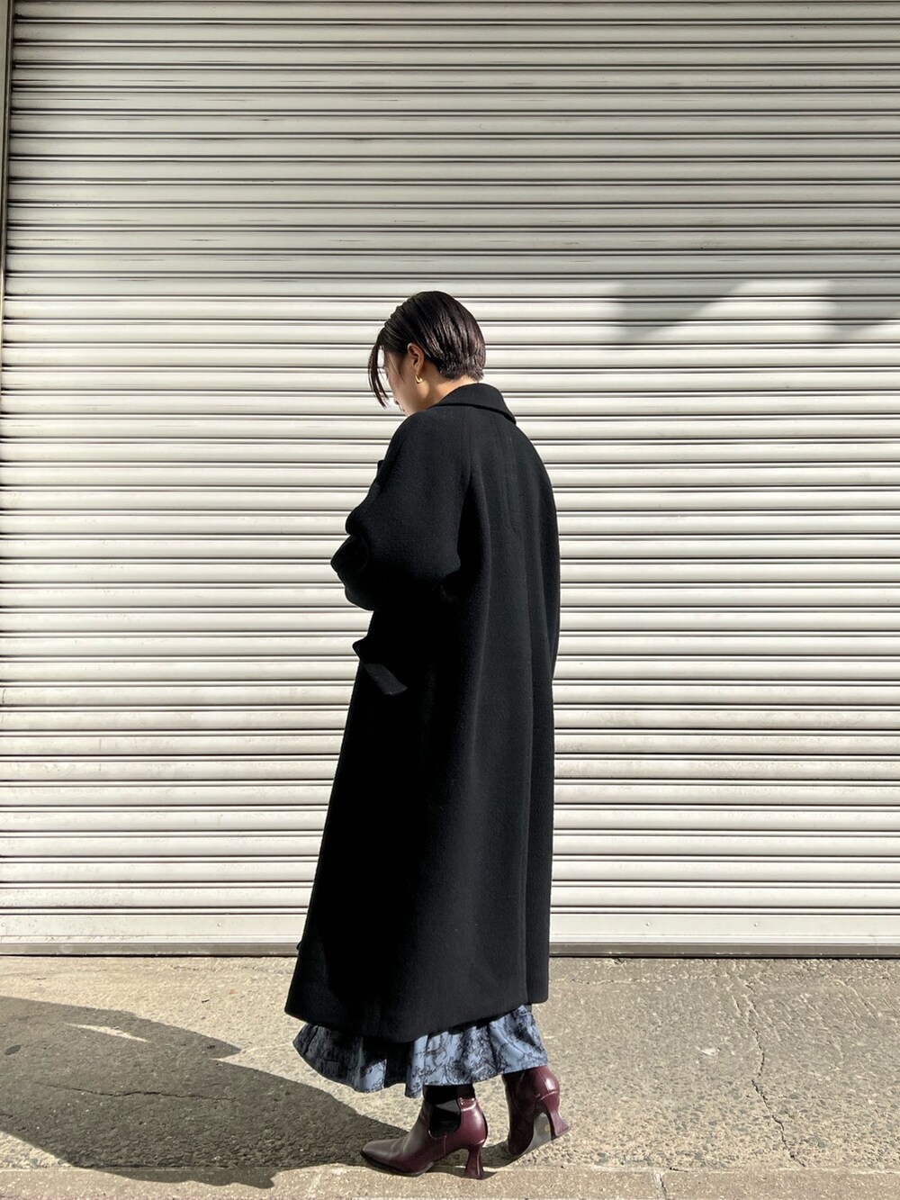 レッド系のブーツ、ブラック系のノーカラーコート、ブルー系のワンピースを着用したレディースの冬コーディネートの2枚目の写真