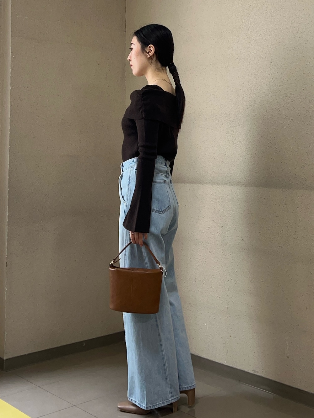 ブルー系のデニムパンツ、ブラウン系のニット/セーター、イエロー系のハンドバッグを着用したレディースの冬コーディネートの2枚目の写真