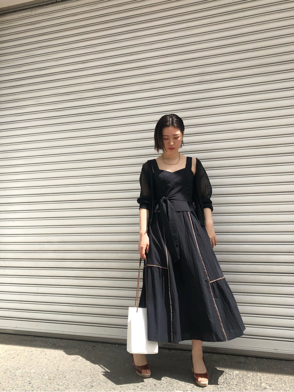 ブラウン系のパンプス、ホワイト系のハンドバッグ、ブラック系のワンピースを着用したレディースの春コーディネートの7枚目の写真