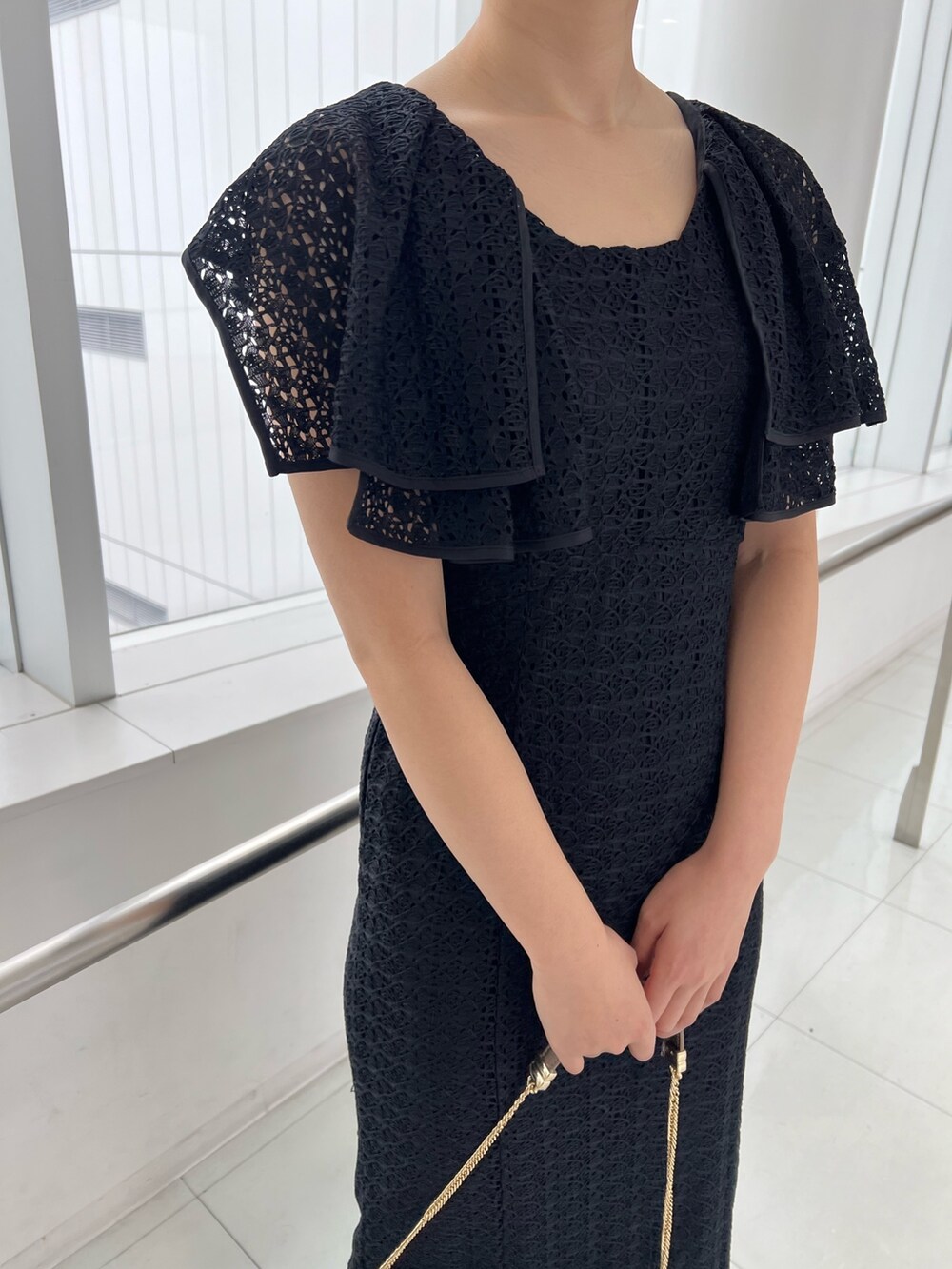 ゴールド系のハンドバッグ、ゴールド系のパンプス、ブラック系のワンピースを着用したレディースの春コーディネートの3枚目の写真