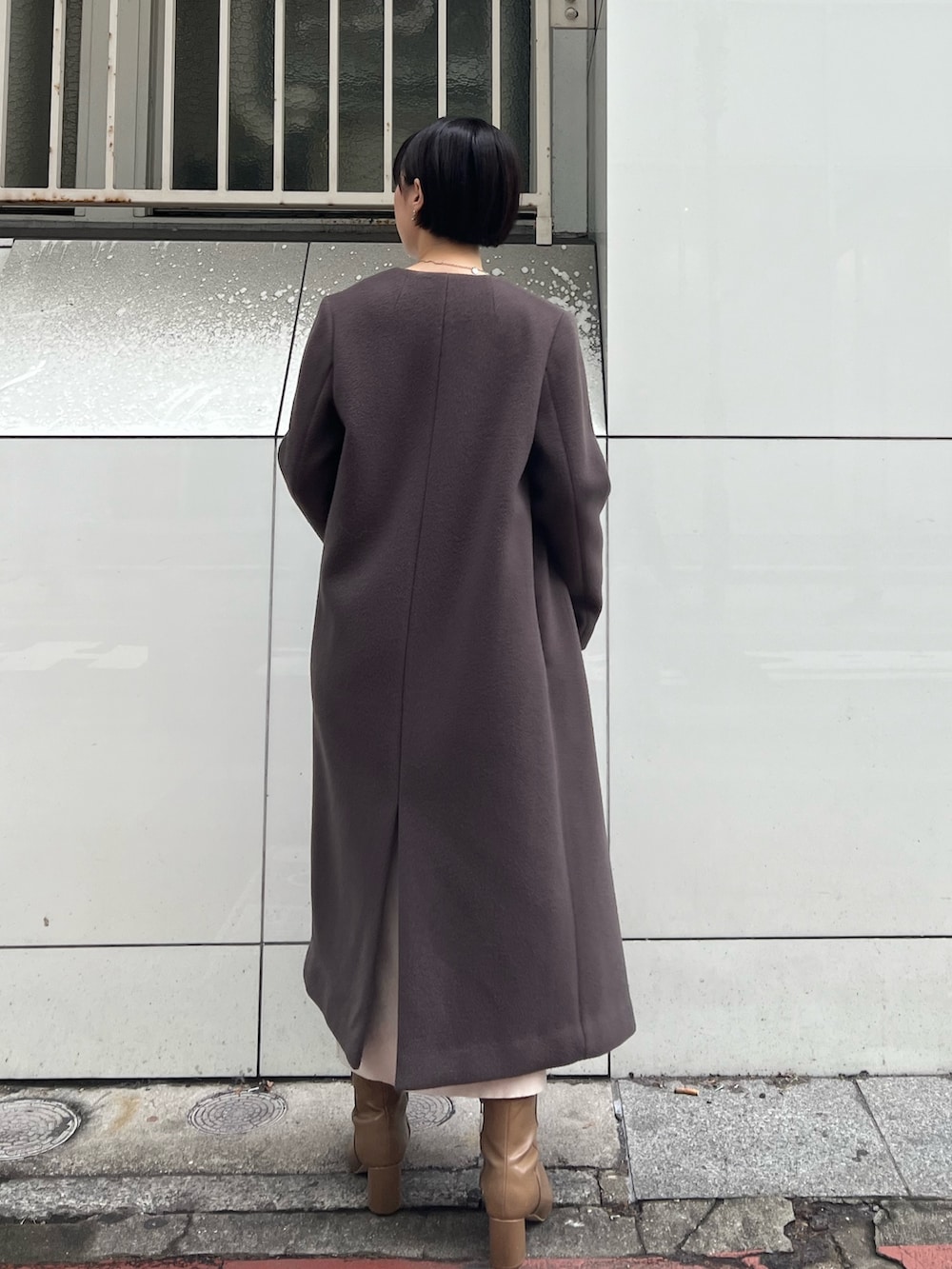 グレー系のノーカラーコート、ベージュ系のブーツ、ホワイト系のハンドバッグを着用したレディースの冬コーディネートの2枚目の写真