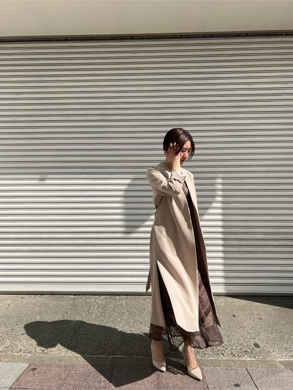 ホワイト系のノーカラーコート、ベージュ系のドレス、ベージュ系のクラッチバッグを着用したレディースの春コーディネートの9枚目の写真