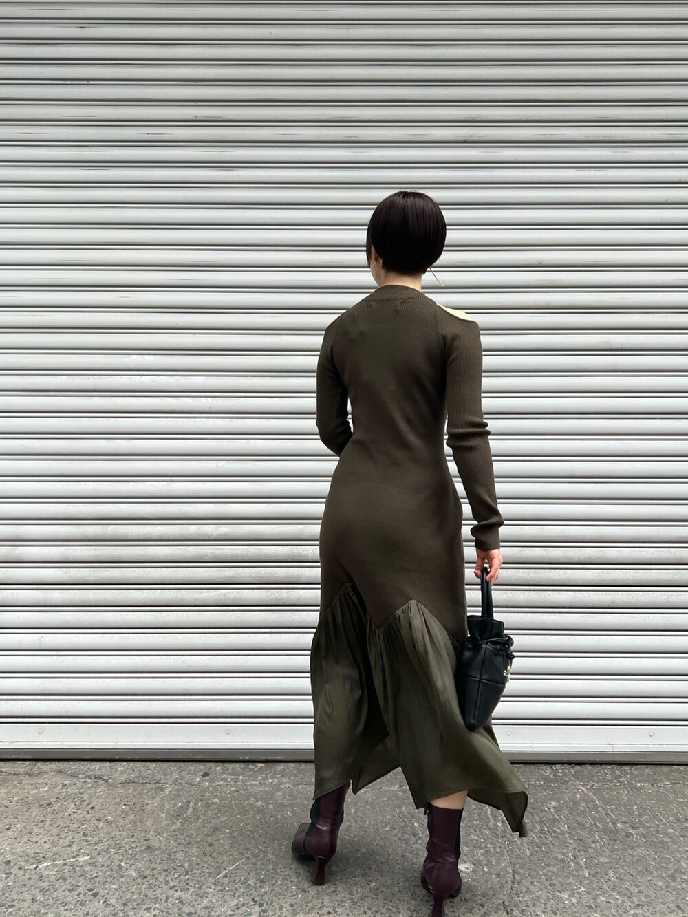 レッド系のブーツ、ブラック系のハンドバッグ、グリーン系のワンピースを着用したレディースの冬コーディネートの3枚目の写真