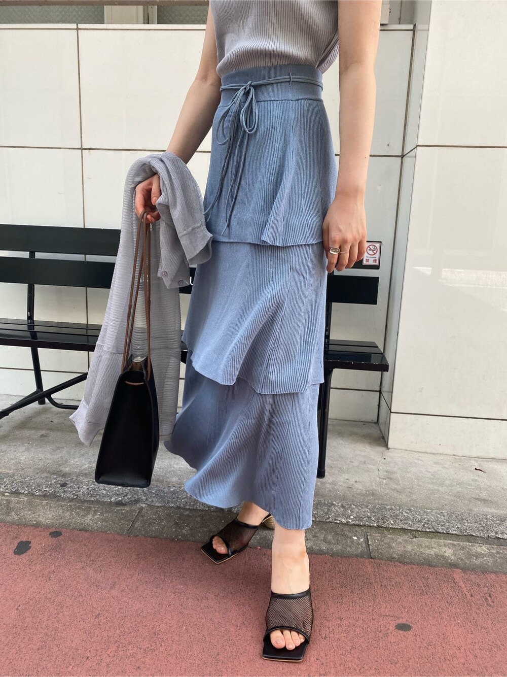 ブラック系のハンドバッグ、ブルー系のスカート、グレー系のニット/セーターを着用したレディースの夏コーディネートの4枚目の写真