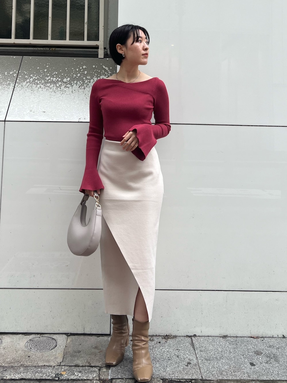 グレー系のノーカラーコート、ベージュ系のブーツ、ホワイト系のハンドバッグを着用したレディースの冬コーディネートの3枚目の写真