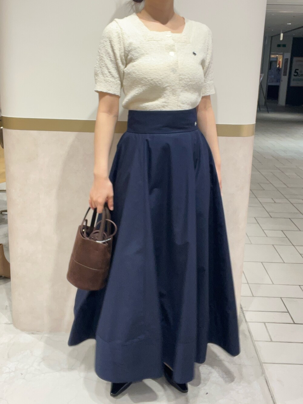 ブルー系のスカート、ホワイト系のニット/セーター、ブラック系のパンプスを着用したレディースの春コーディネートの4枚目の写真
