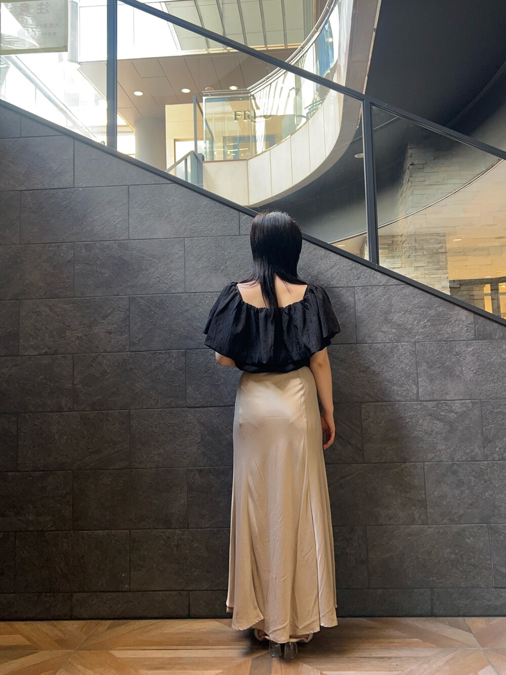 ブラック系のシャツ/ブラウス、ベージュ系のスカート、ホワイト系のサンダルを着用したレディースの夏コーディネートの3枚目の写真