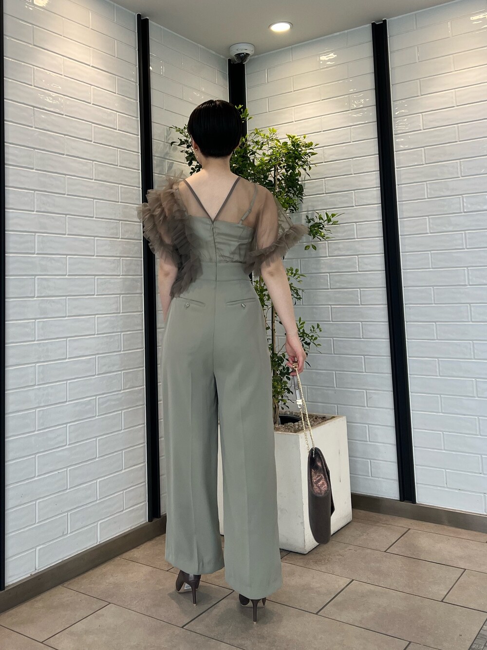 シルバー系のパンプス、シルバー系のハンドバッグ、グリーン系のパンツドレスを着用したレディースの春コーディネートの3枚目の写真