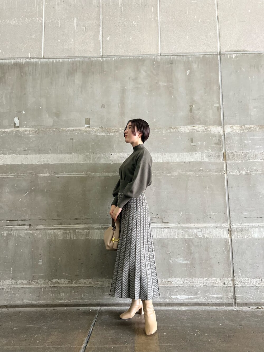 ベージュ系のブーツ、ベージュ系のハンドバッグ、ベージュ系のワンピースを着用したレディースの秋コーディネートの2枚目の写真