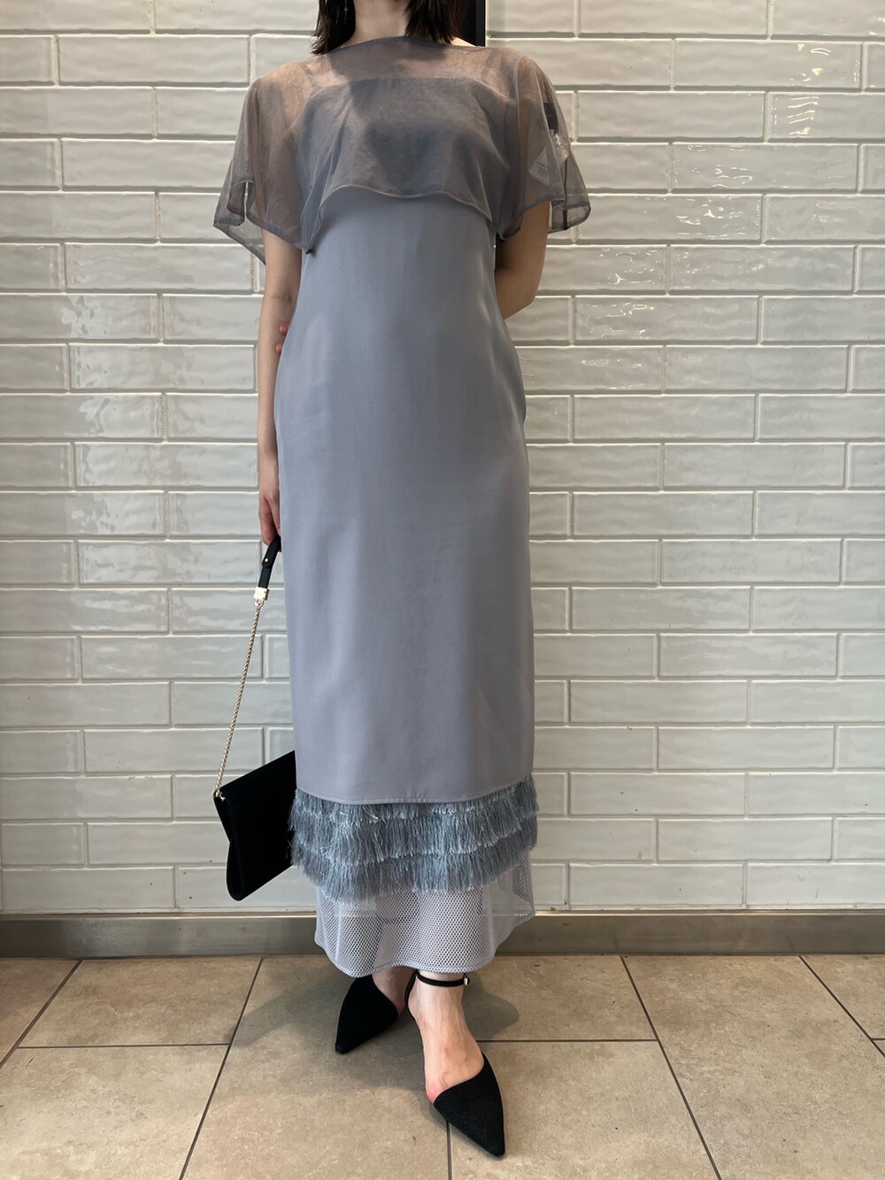 パープル系のドレス、ブラック系のクラッチバッグ、ブラック系のパンプスを着用したレディースの秋コーディネートの5枚目の写真