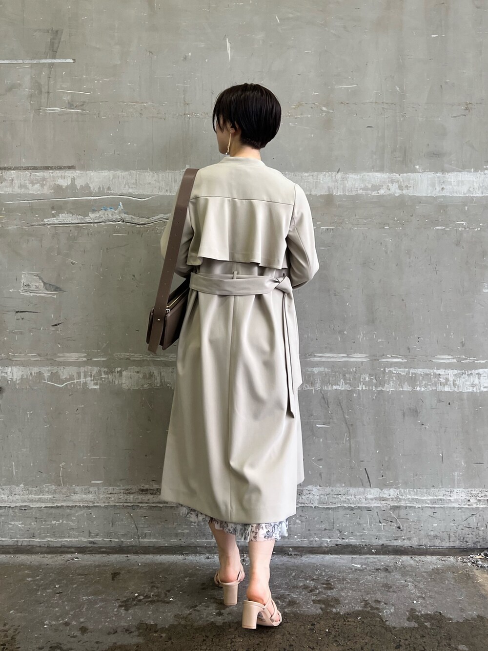 ベージュ系のノーカラーコート、ホワイト系のスカート、ベージュ系のサンダルを着用したレディースの冬コーディネートの2枚目の写真