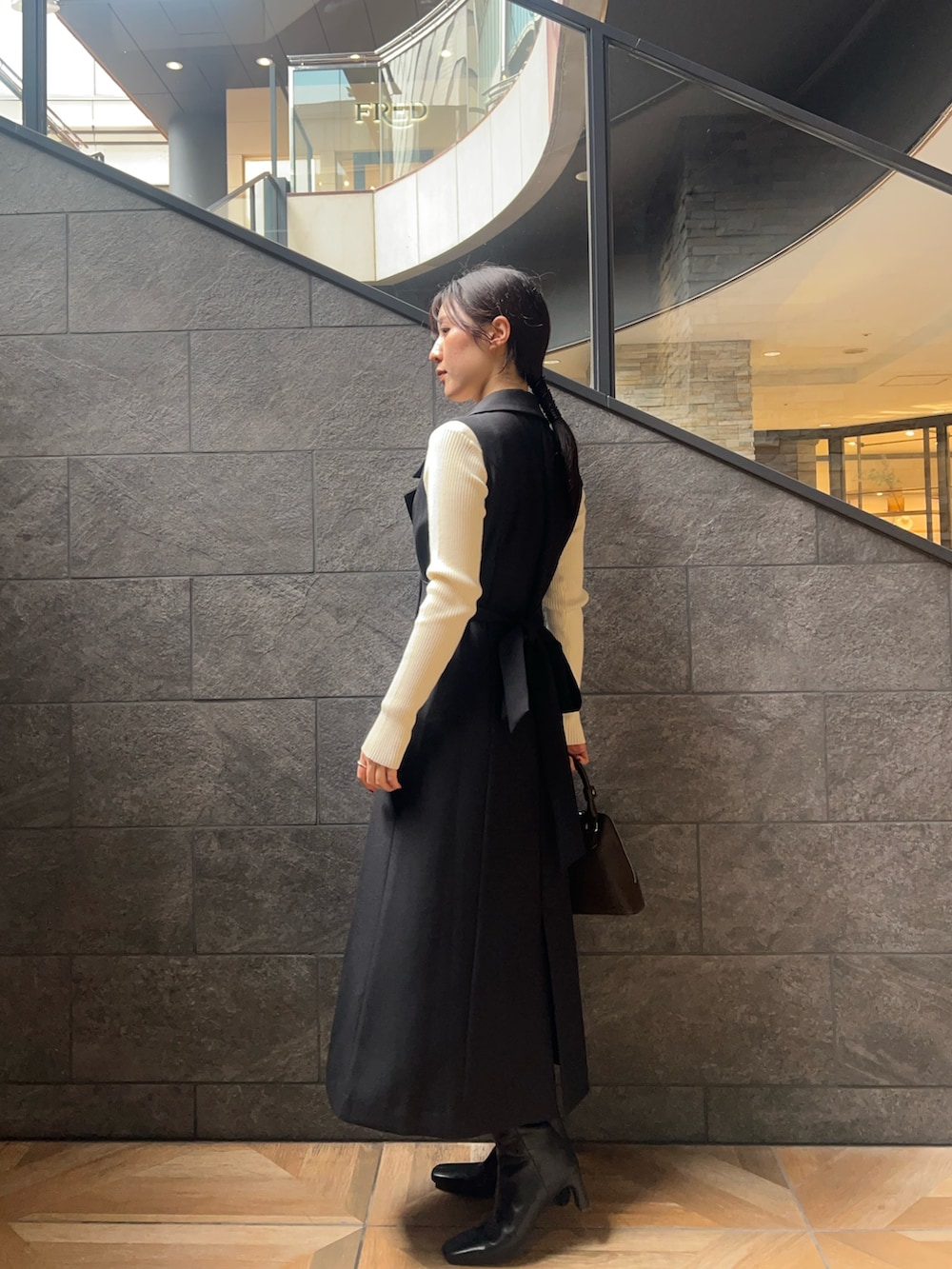 ブラック系のワンピース、ホワイト系のニット/セーター、ブラック系のブーツを着用したレディースの秋コーディネートの2枚目の写真