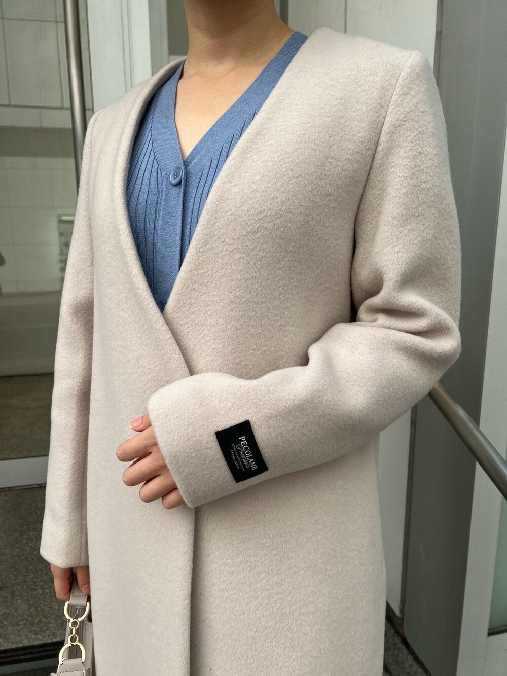 ベージュ系のブーツ、ホワイト系のハンドバッグ、ホワイト系のノーカラーコートを着用したレディースの冬コーディネートの4枚目の写真