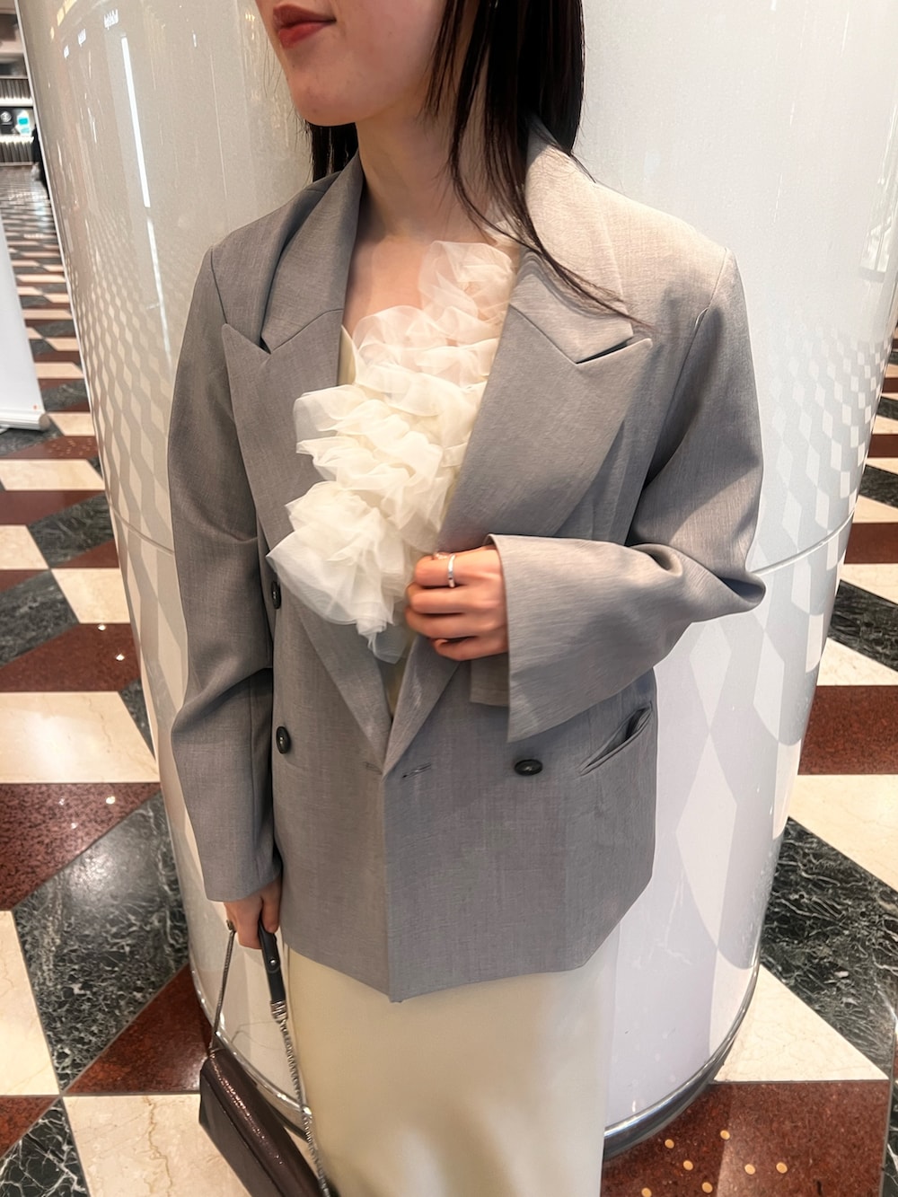 グレー系のテーラードジャケット、イエロー系のドレス、シルバー系のクラッチバッグを着用したレディースの冬コーディネートの6枚目の写真