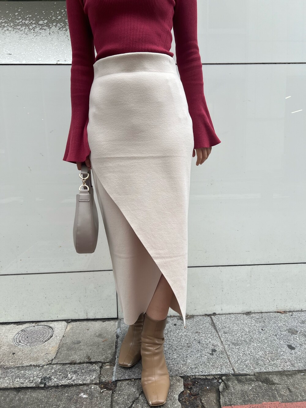 グレー系のノーカラーコート、ベージュ系のブーツ、ホワイト系のハンドバッグを着用したレディースの冬コーディネートの6枚目の写真